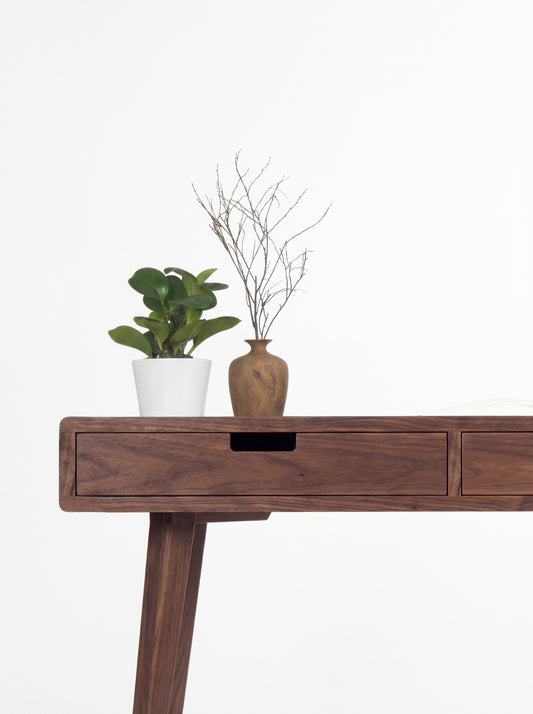 Close-up of the HEIM 140 desk in solid walnut, showing a drawer's cut-out grip and the leg below