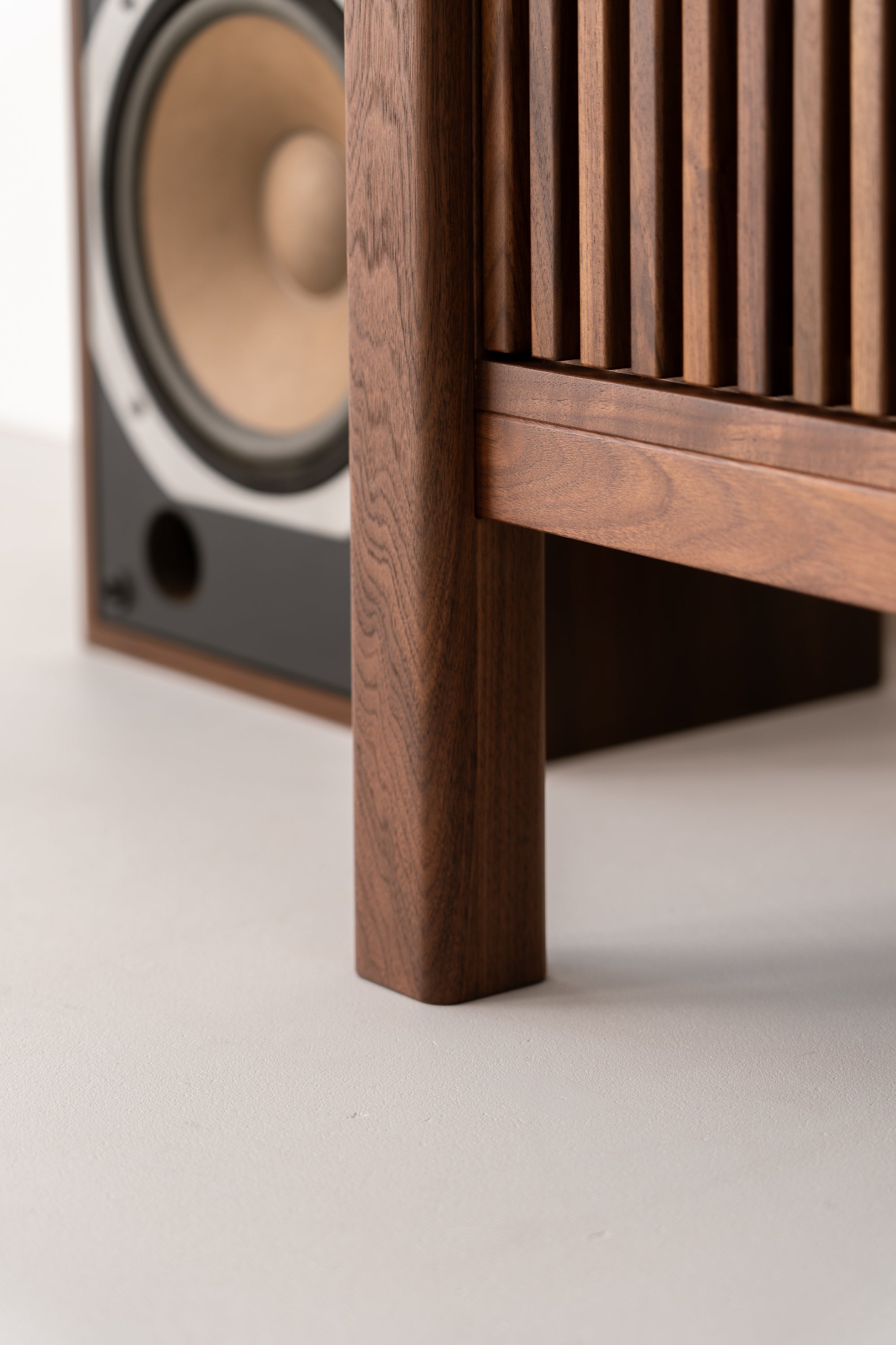 Close-up of a wooden speaker cabinet and speaker on a light-colored floor.