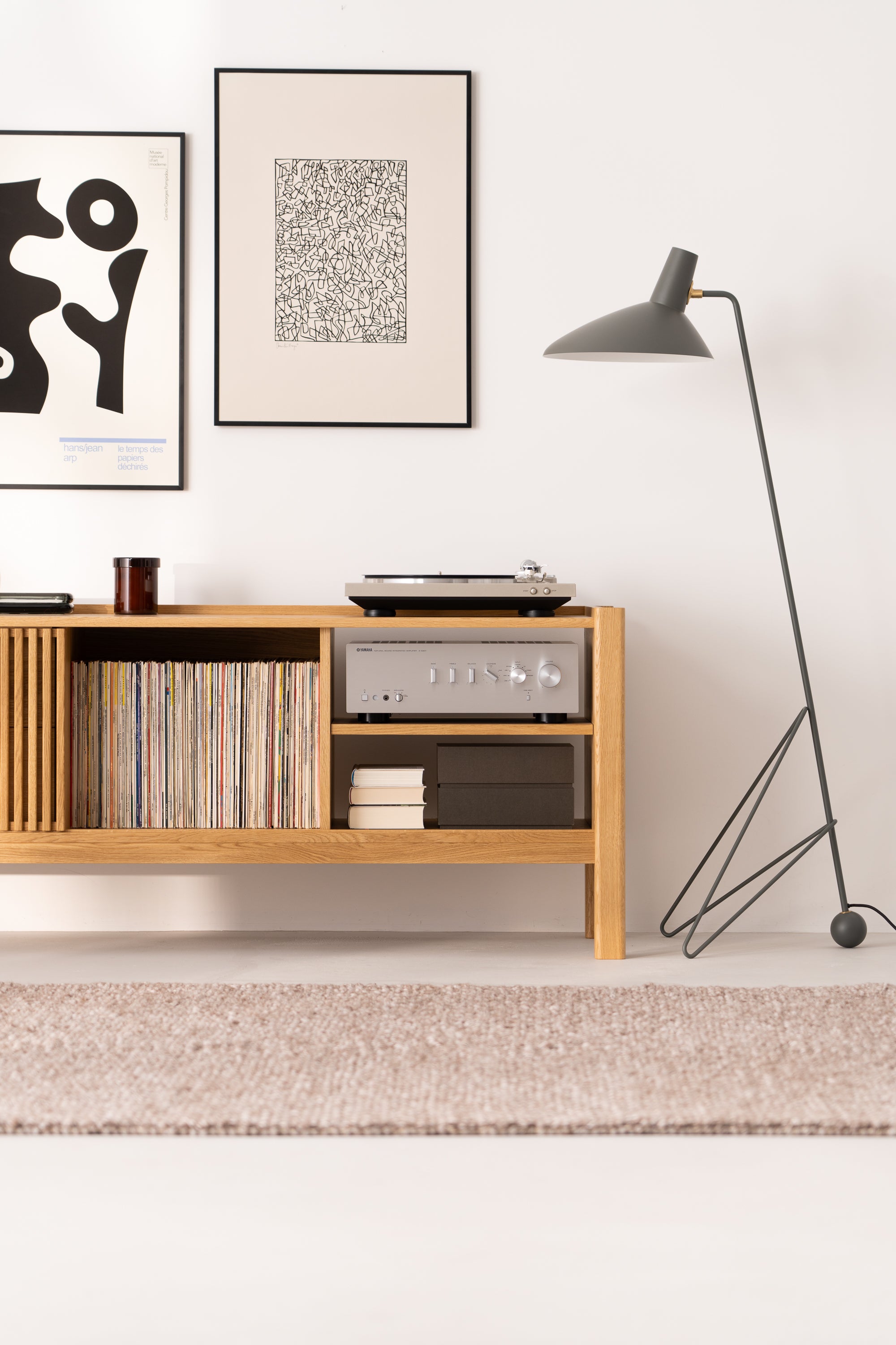 Modern living room with a wooden record shelf, turntable, abstract art, and a floor lamp.
