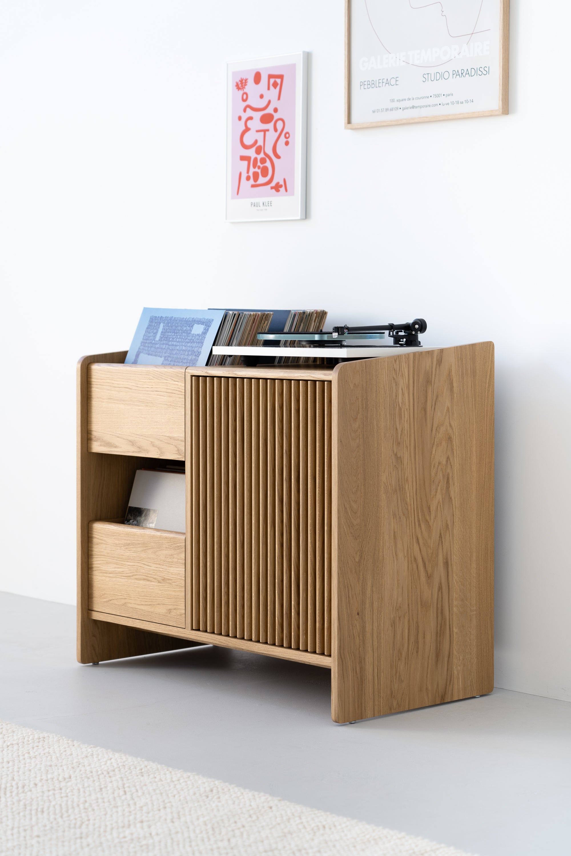 Wooden record cabinet with vinyl records and a turntable, adorned with abstract art on a white wall.