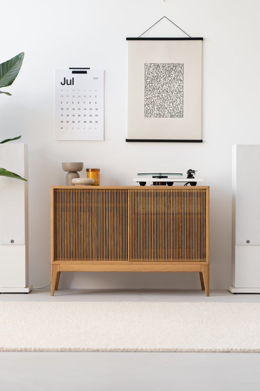 Minimalist living room with a wooden sideboard, wall calendar, abstract art, and decorative items.