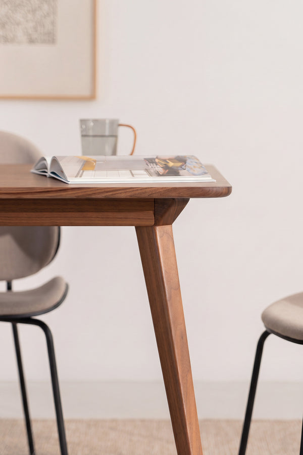 Wooden table with an open magazine, a mug, and two chairs in a minimalist room.