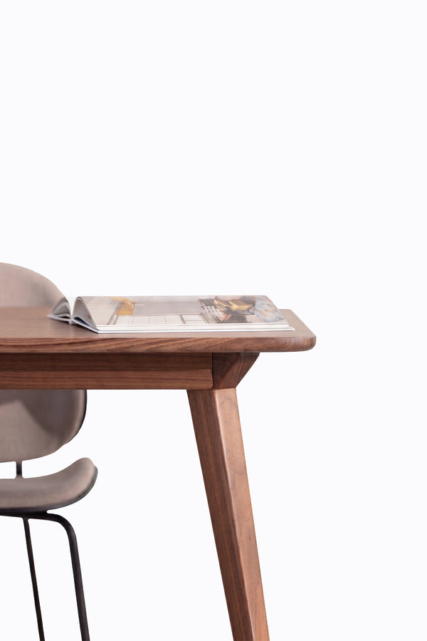 Wooden table with an open magazine on top, next to a beige chair.