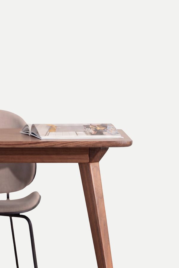 Wooden table with an open magazine on top, next to a beige chair.