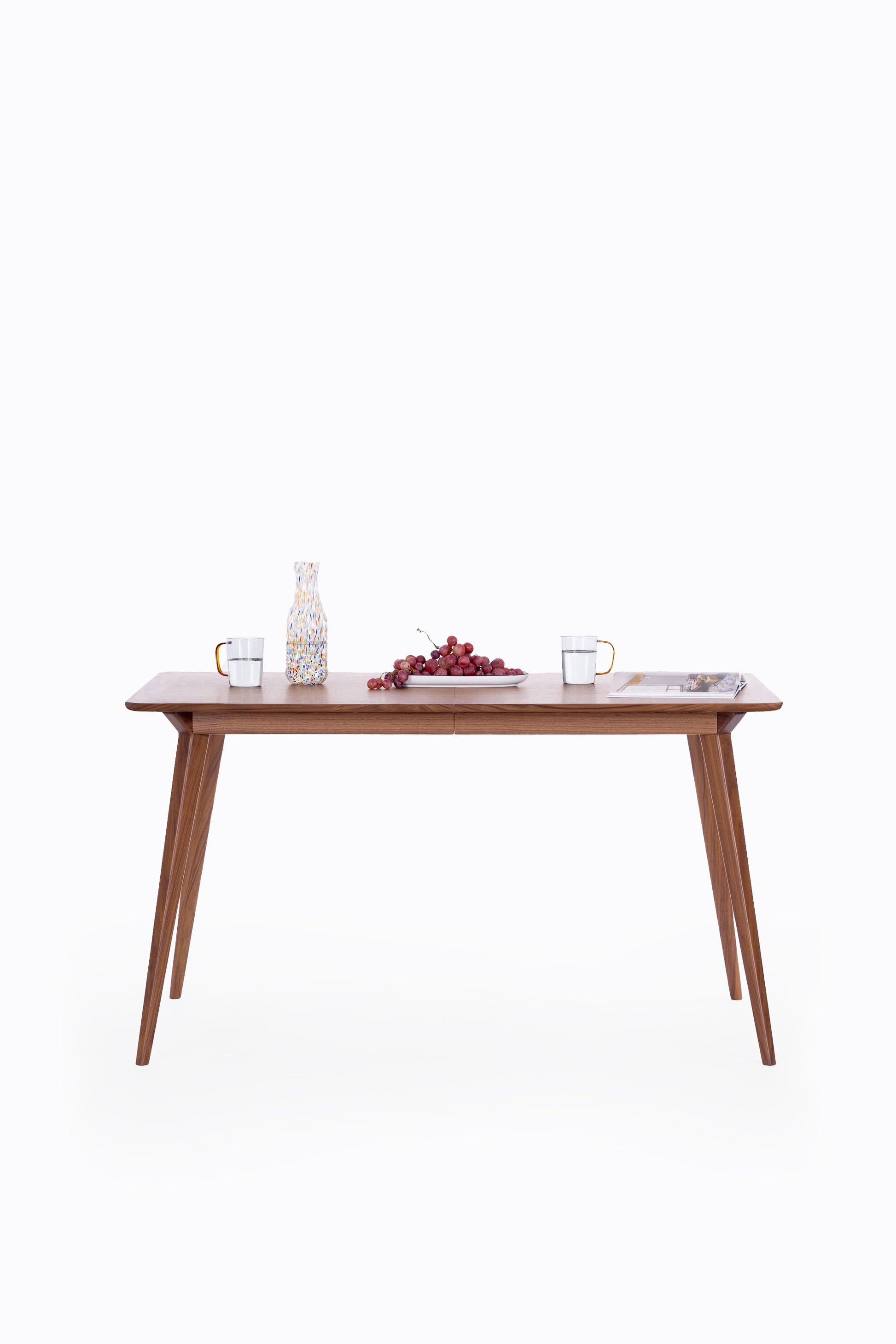 Wooden table with water glasses, grapes, and a magazine on a white background.