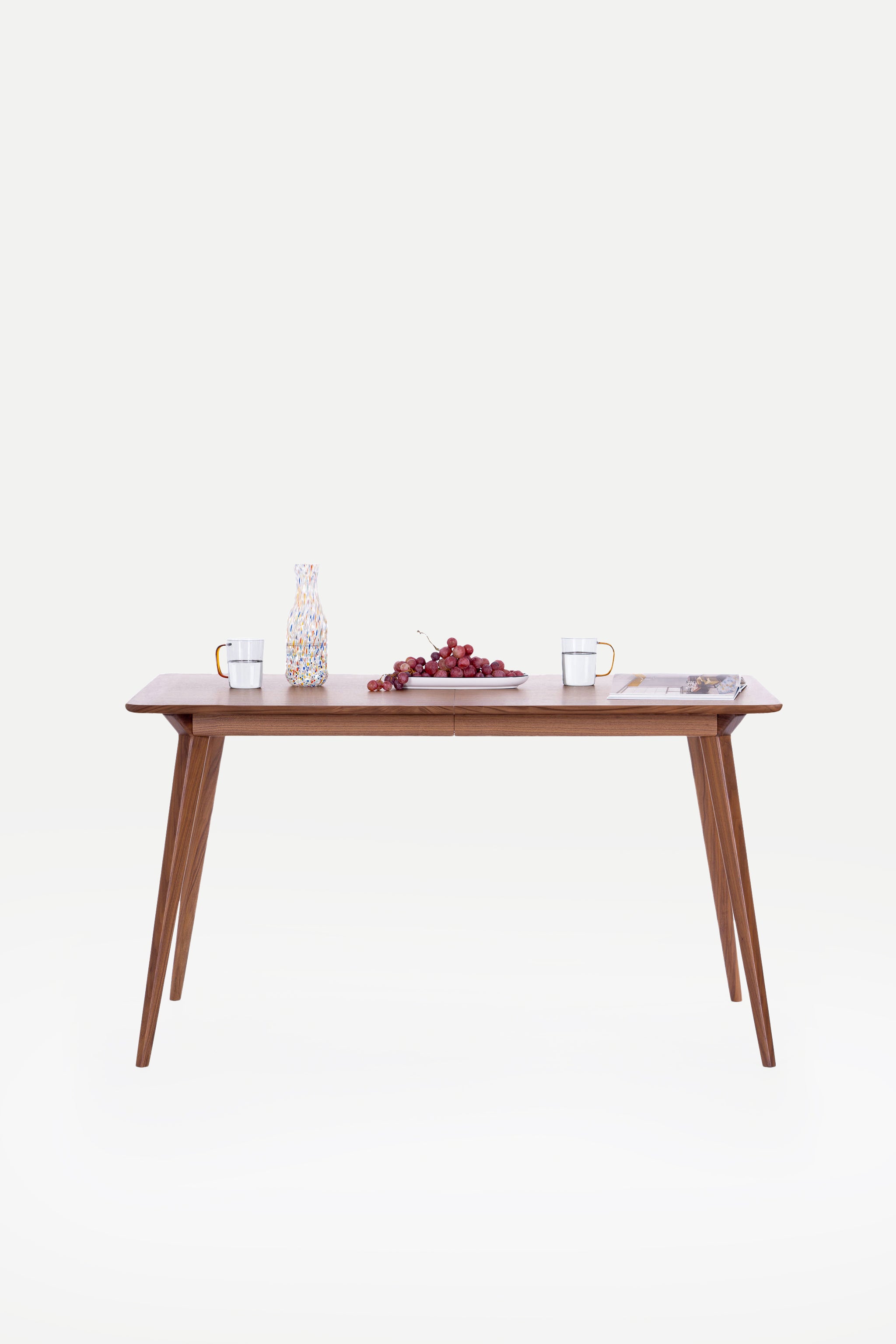Wooden table with water glasses, grapes, and a magazine on a white background.