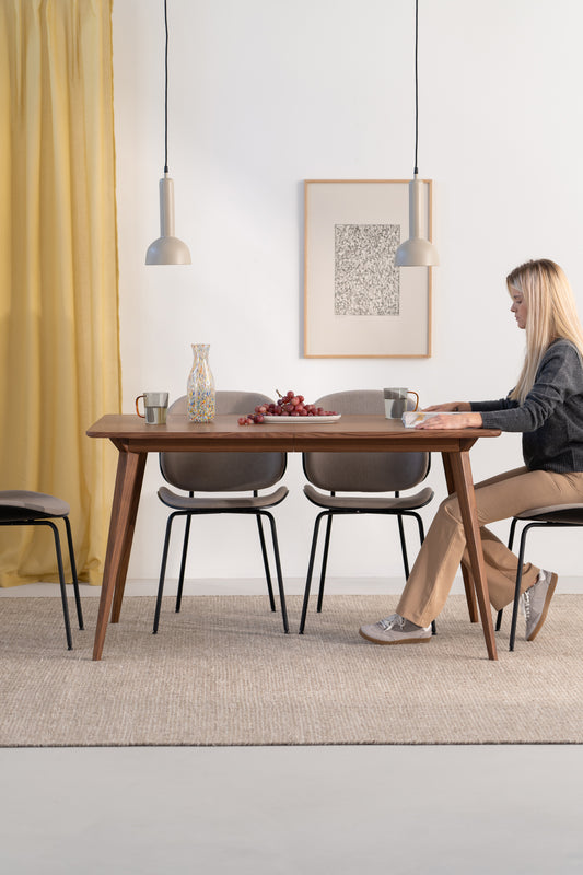 A woman sits at a modern dining table with chairs, pendant lights, and a plate of grapes.