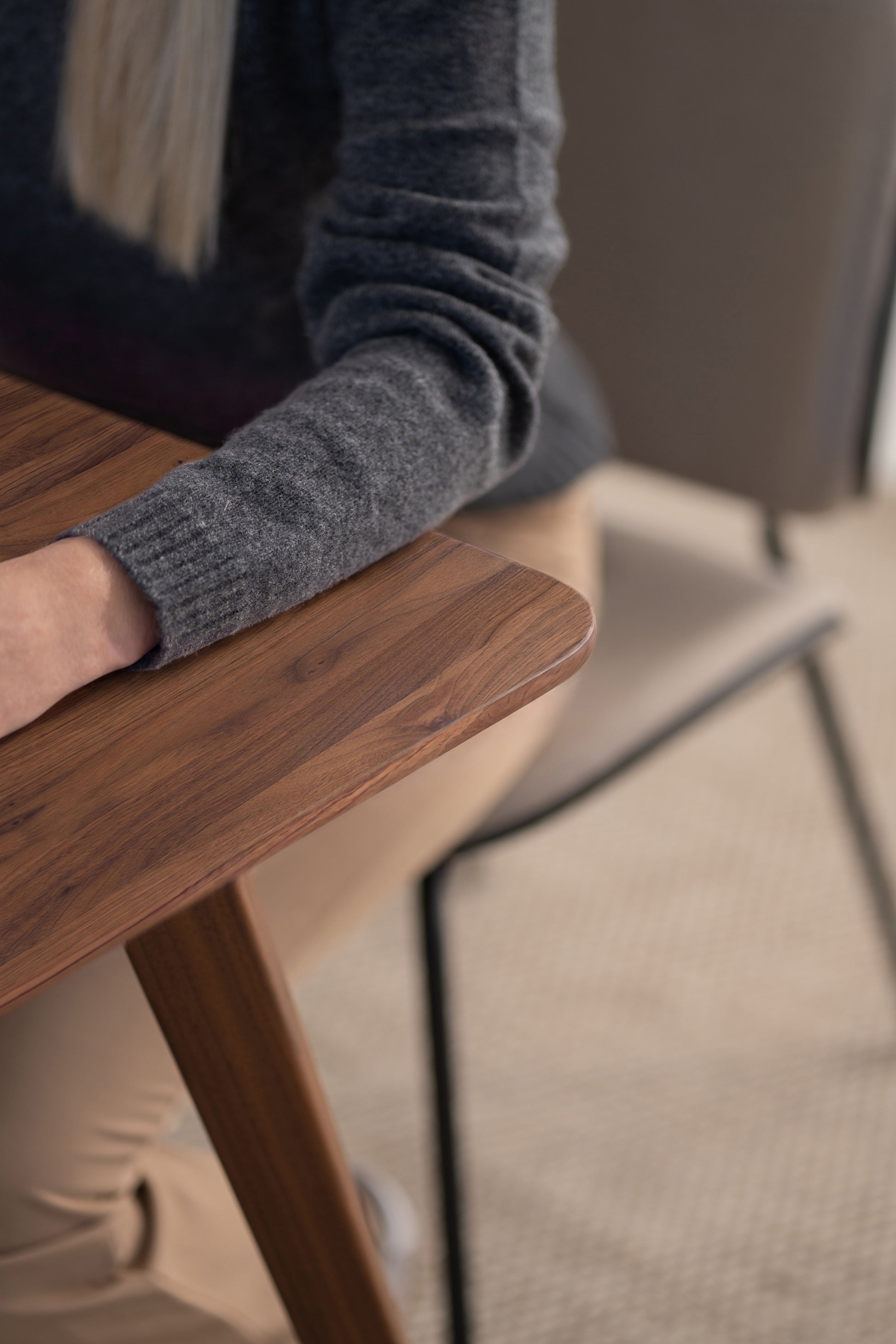 Person in a grey sweater sitting at a wooden table with a beige chair.
