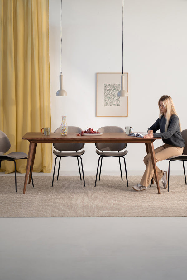 Woman reading at a wooden dining table with chairs, pendant lights, and yellow curtains.
