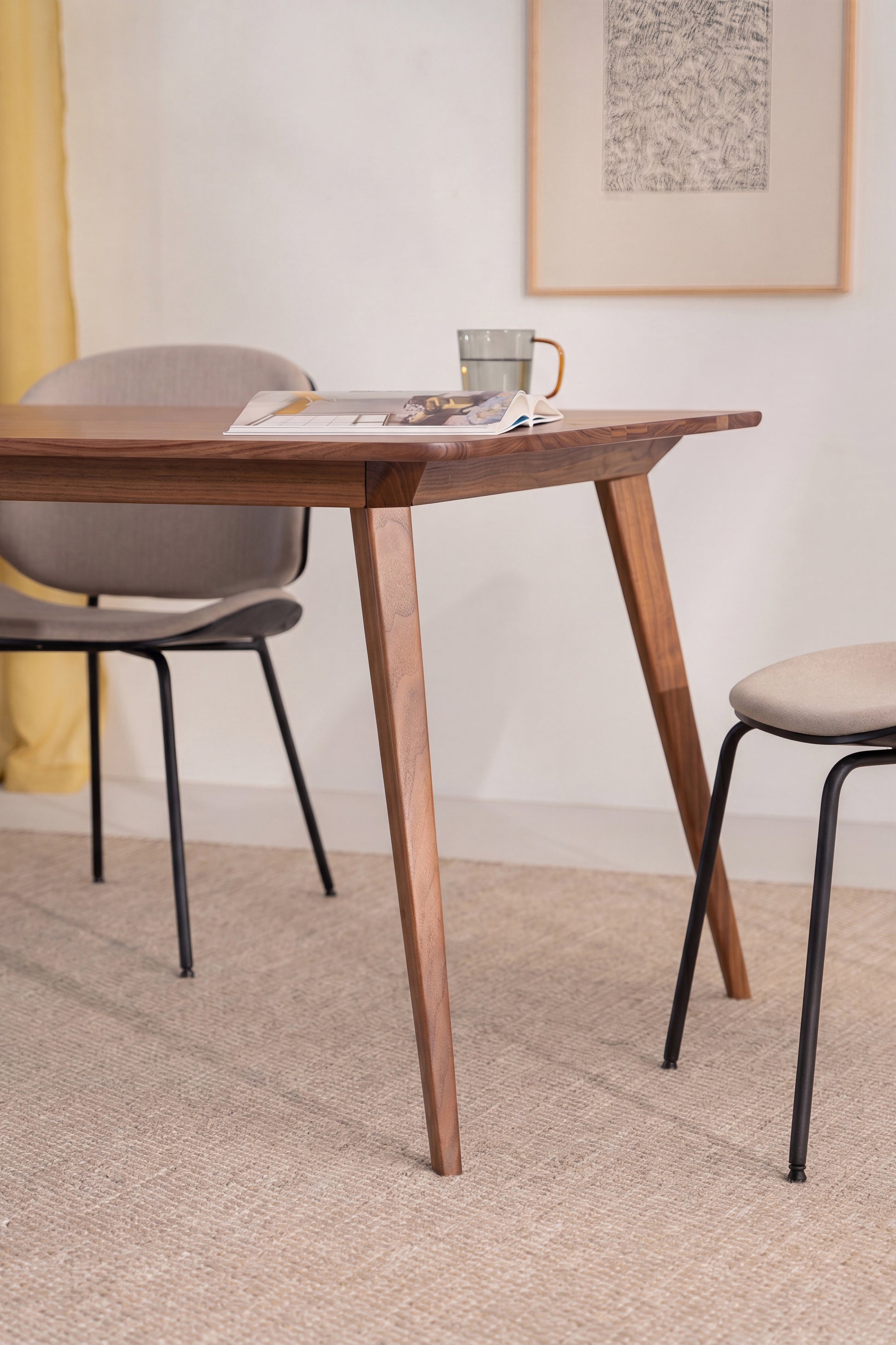 Wooden table with an open book and mug, surrounded by two chairs in a minimalist room setting.