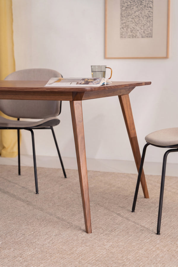 Wooden table with an open book and mug, surrounded by two chairs in a minimalist room setting.