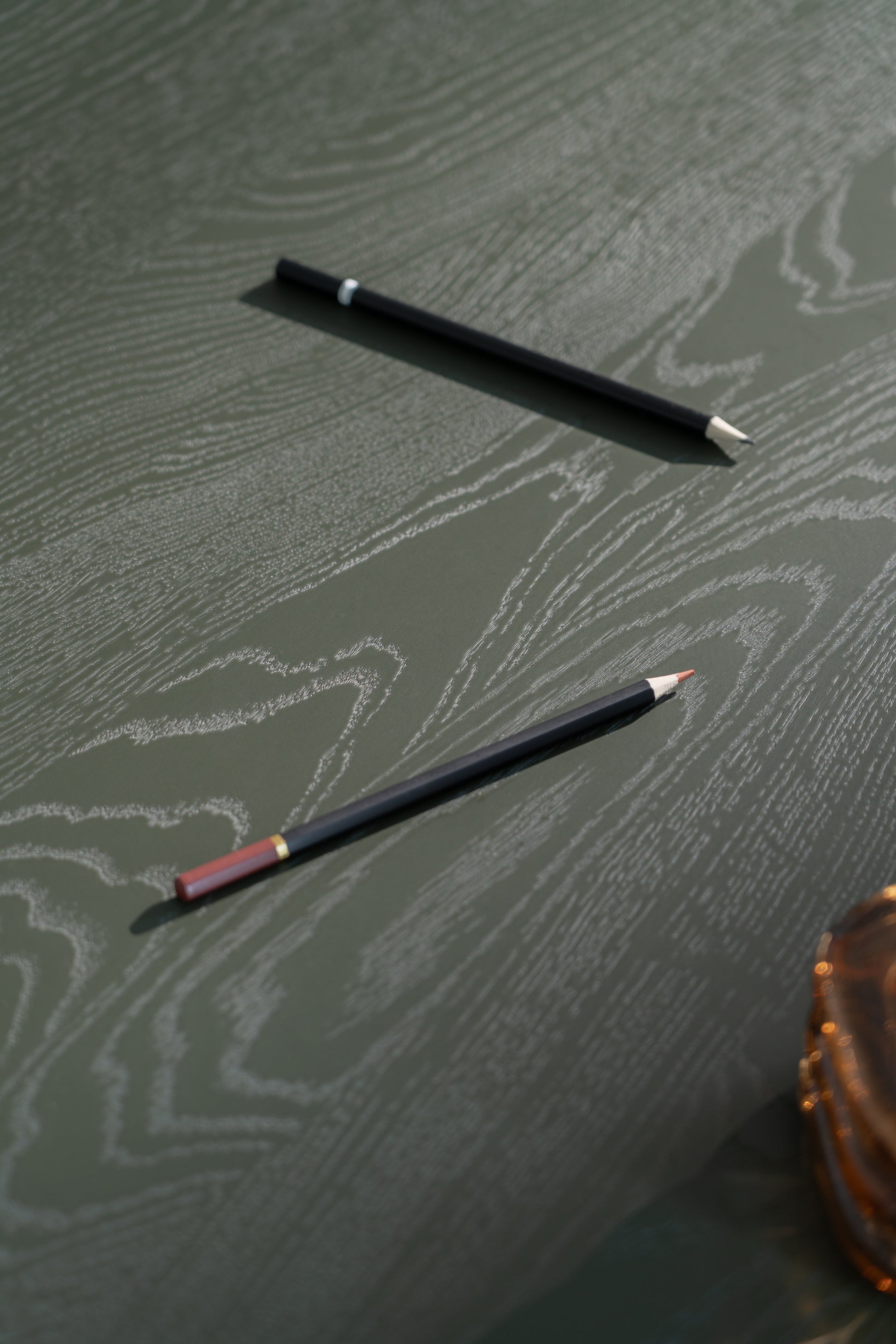 Close-up of the edge where the dark green finish meets the natural oak on the NOON table