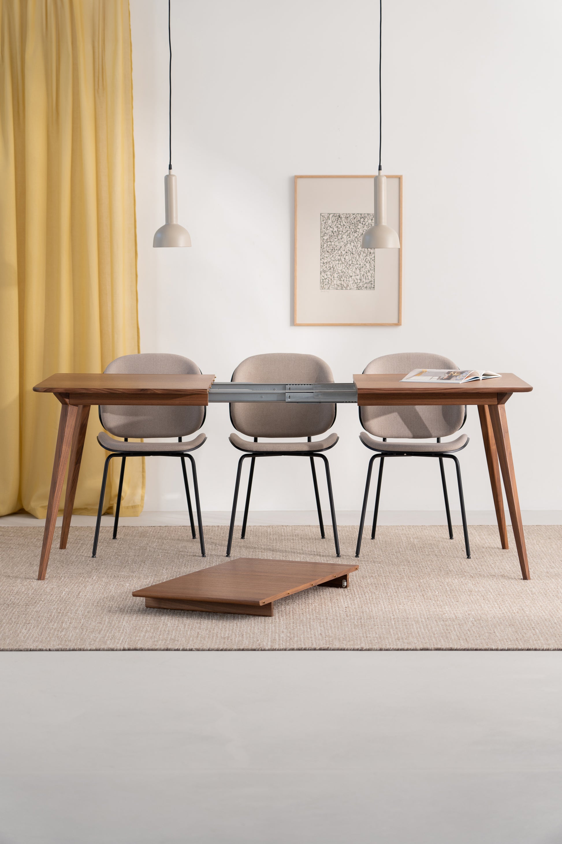 Minimalist dining setup with three chairs, a partially assembled table, pendant lights, and yellow curtains.