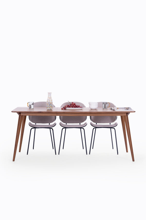 Dining table with three chairs, decorated with grapes, a vase, mugs, and bowls on a clean, white background.