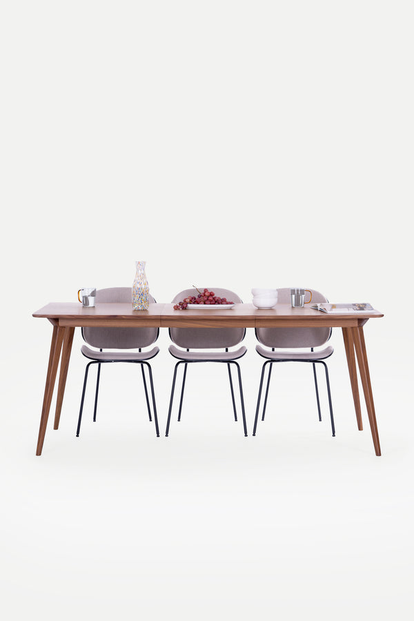 Dining table with three chairs, decorated with grapes, a vase, mugs, and bowls on a clean, white background.