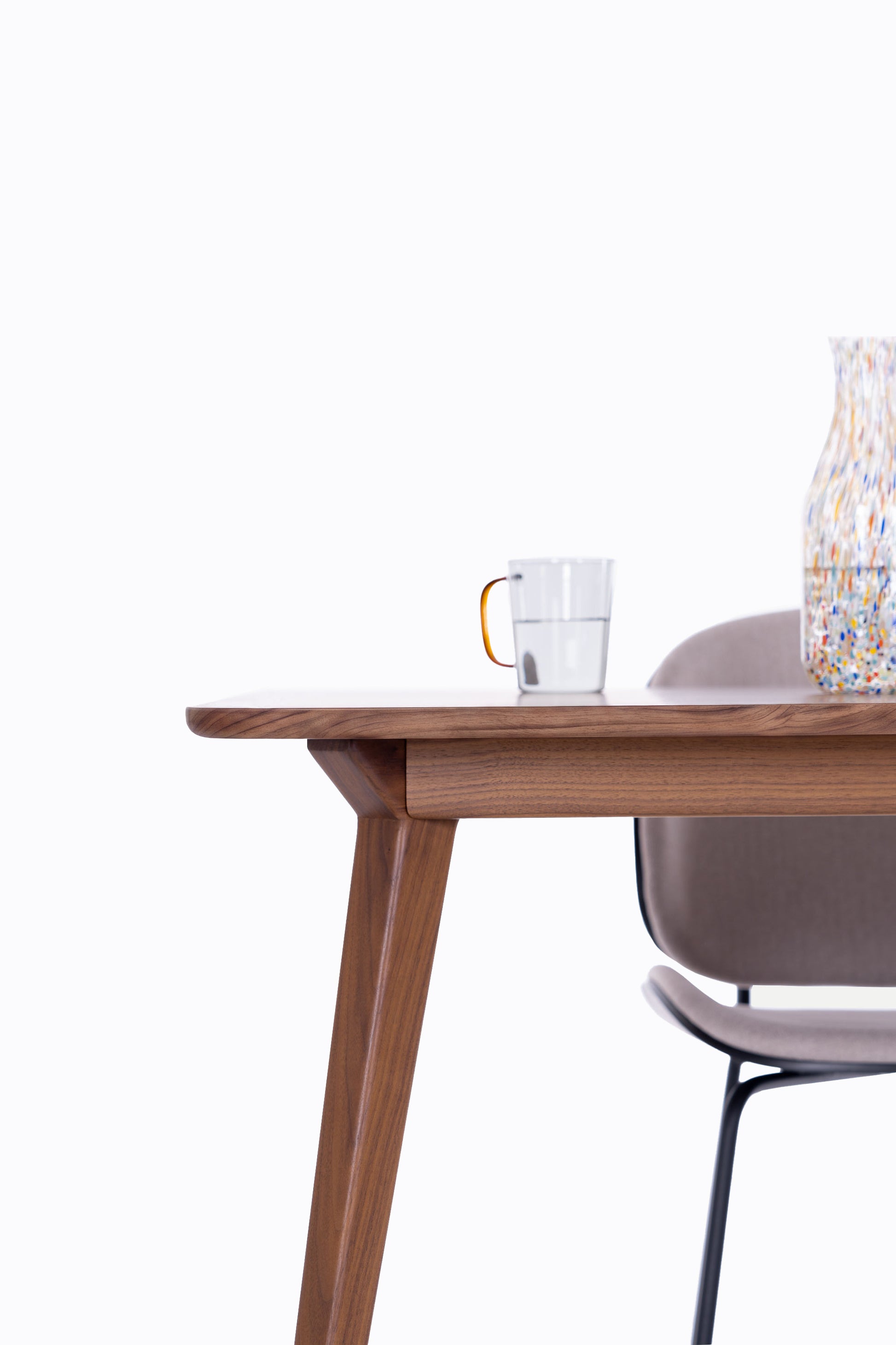 Wooden table with a cup and chair nearby against a light background.
