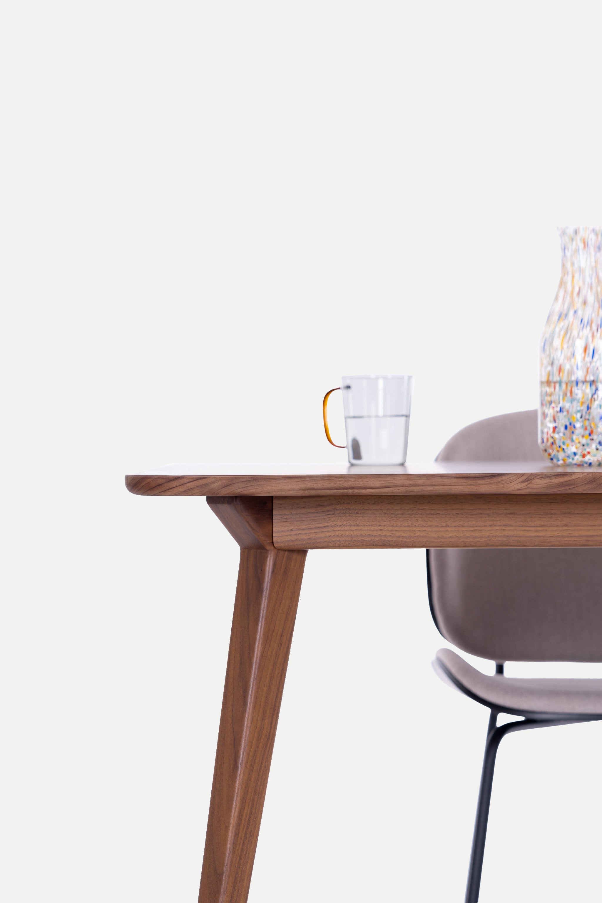 Wooden table with a cup and chair nearby against a light background.
