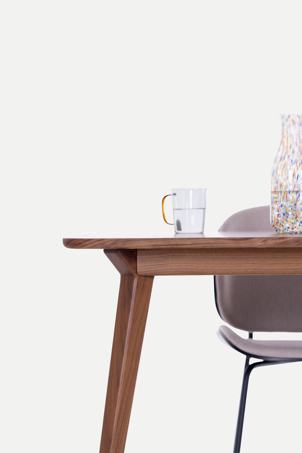 Wooden table with a cup and chair nearby against a light background.