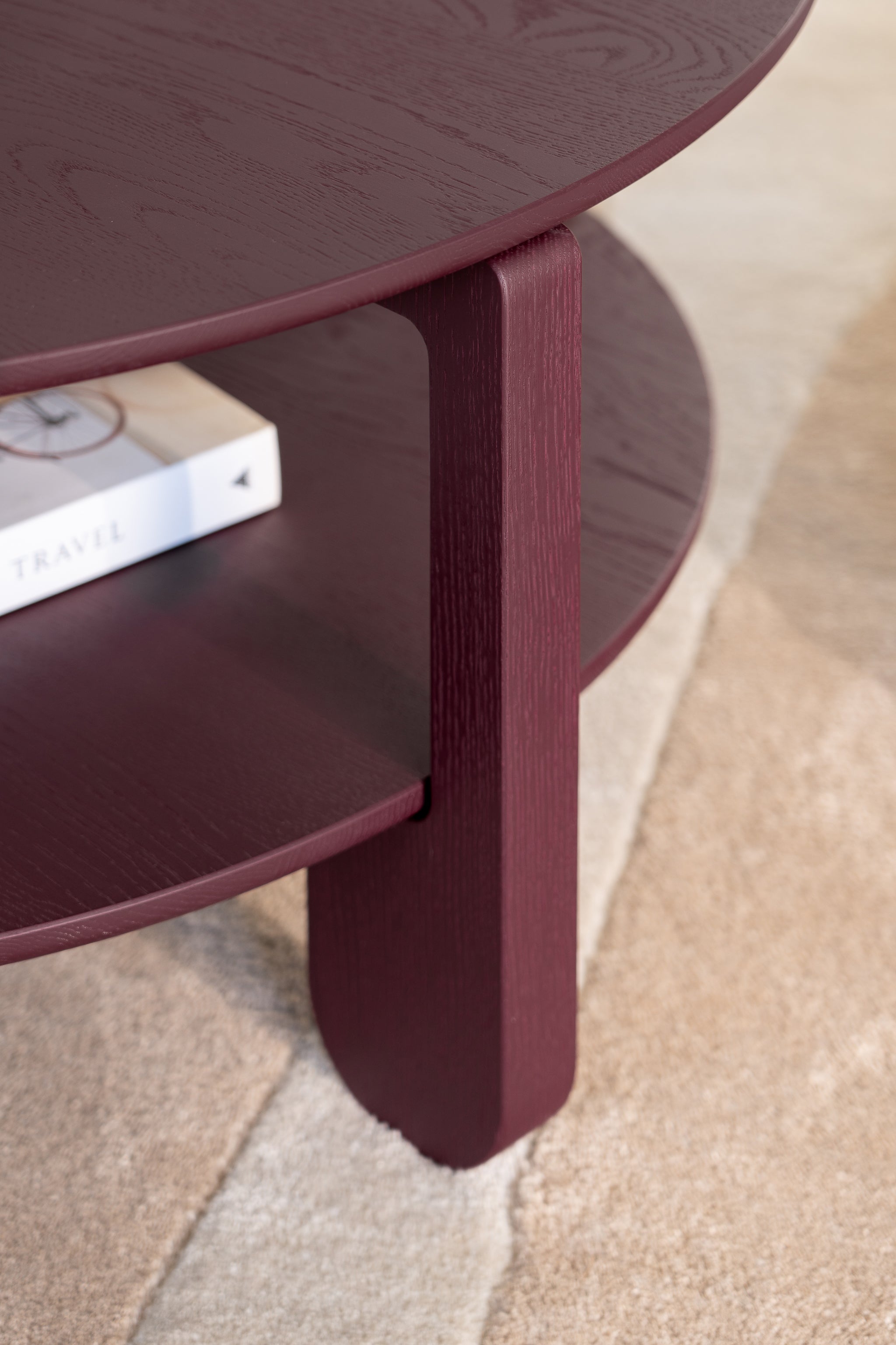 Side profile of the burgundy NOON coffee table showing tapered oak legs and round top