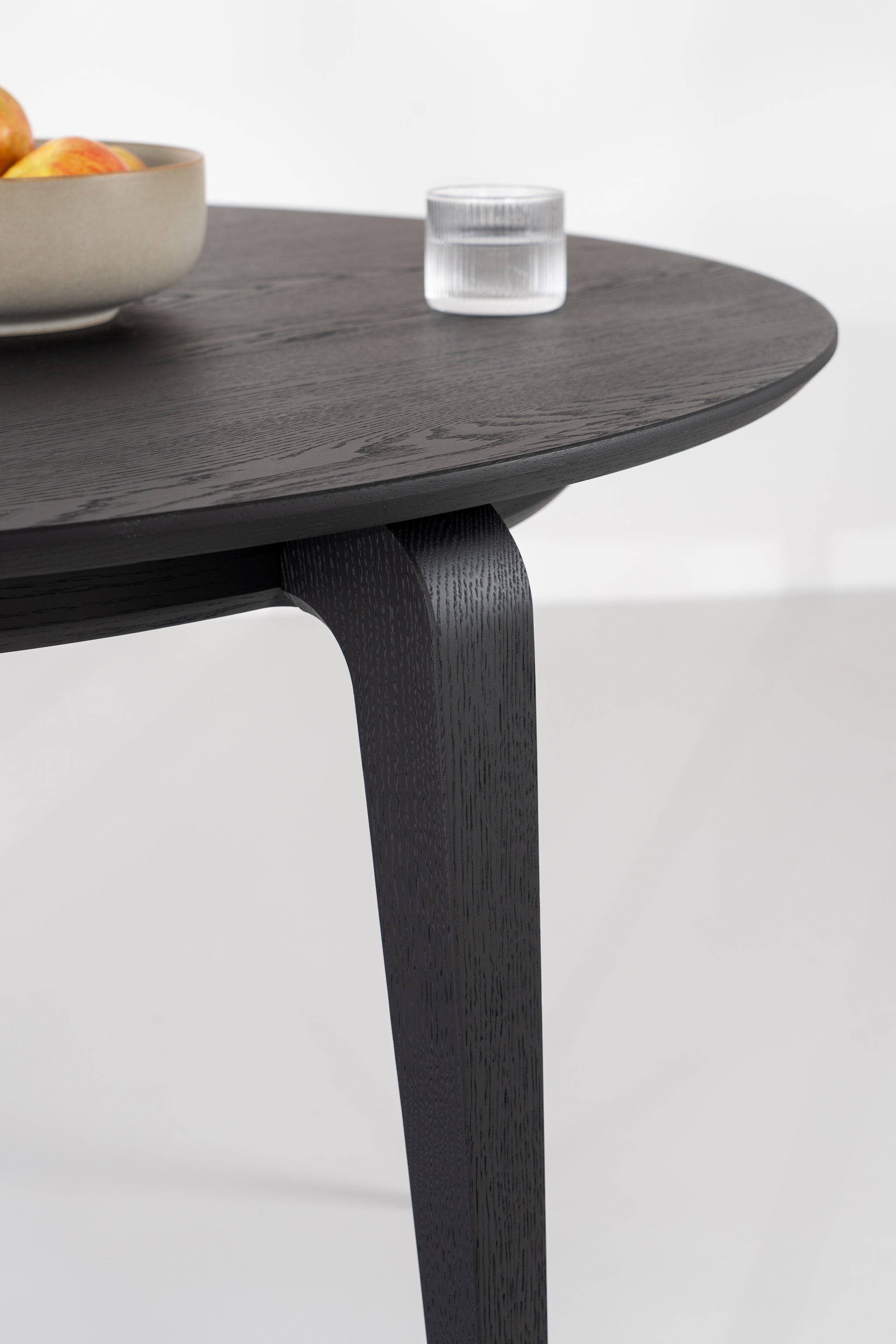YUKI round dining table in black oak, front view on light wooden floor