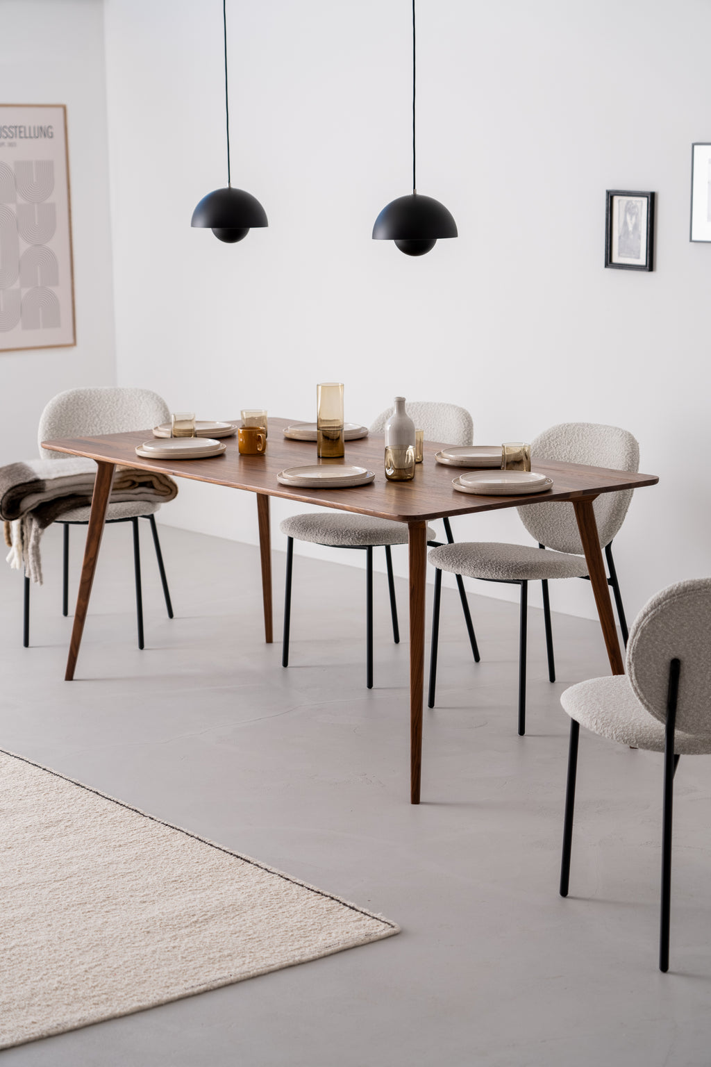 A wooden table set with tableware, surrounded by white chairs in a modern interior with two hanging lamps.