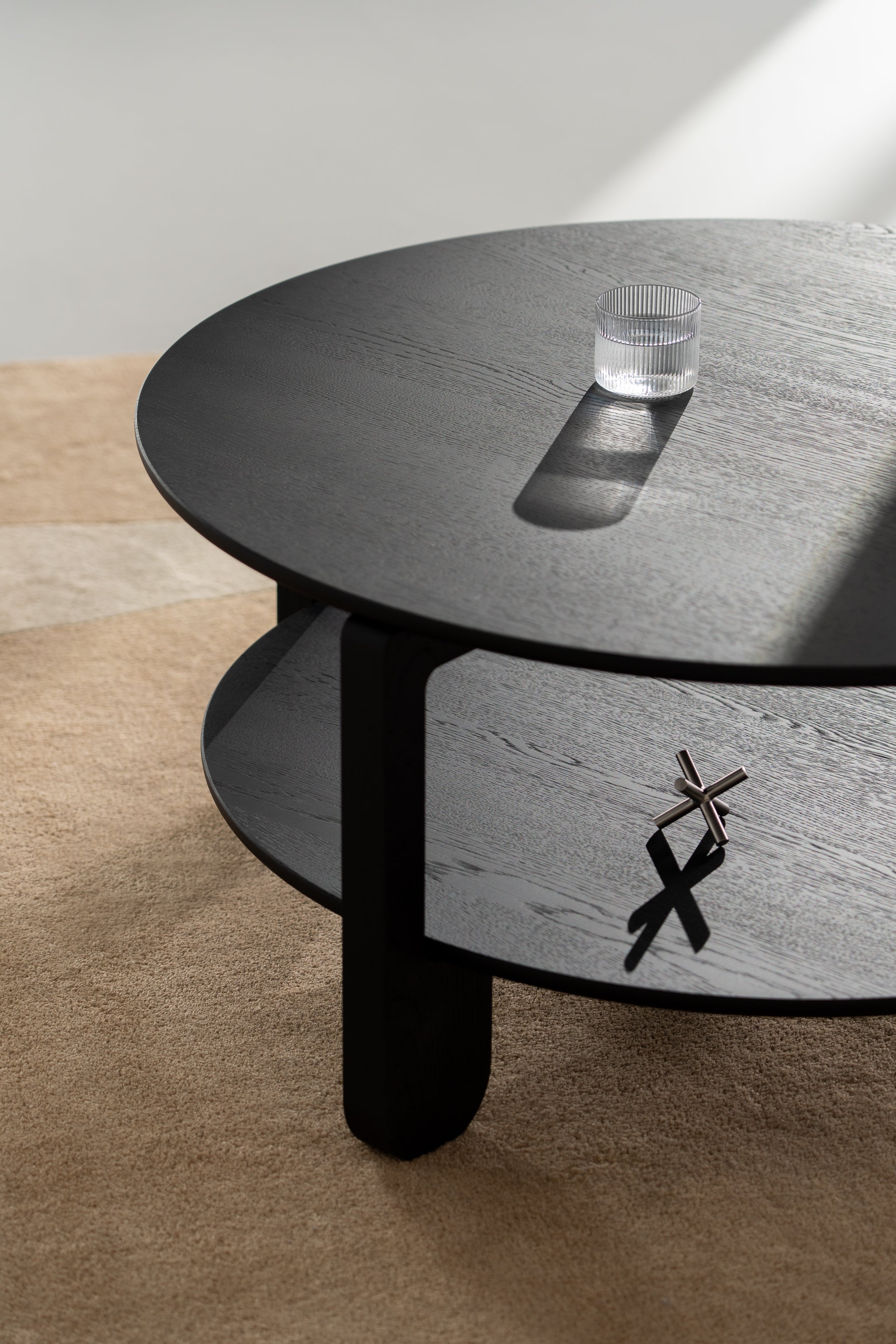 Angled view of the NOON table highlighting tapered legs and round tabletop in black oak