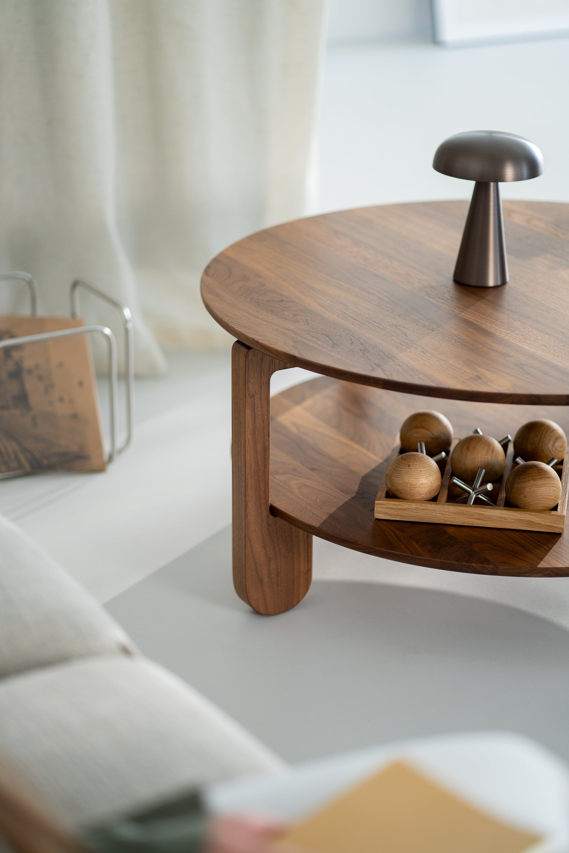 Side profile of the round NOON table in dark walnut against a neutral wall