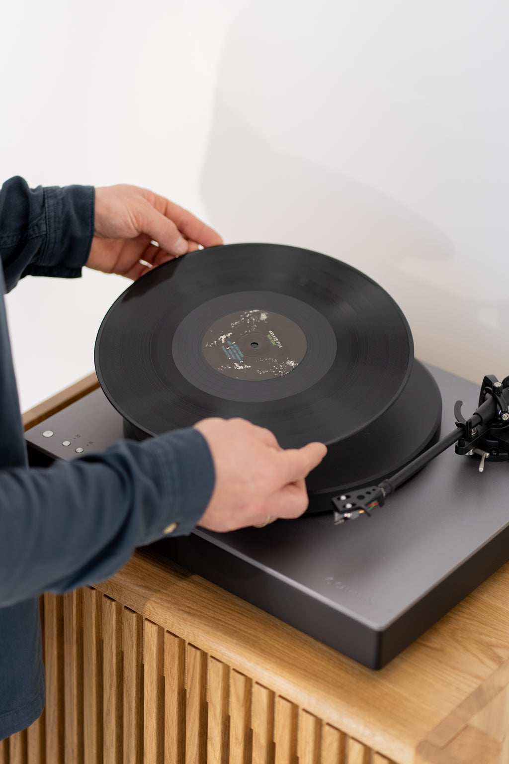 Hands placing a vinyl record onto a turntable on a solid oak cabinet.