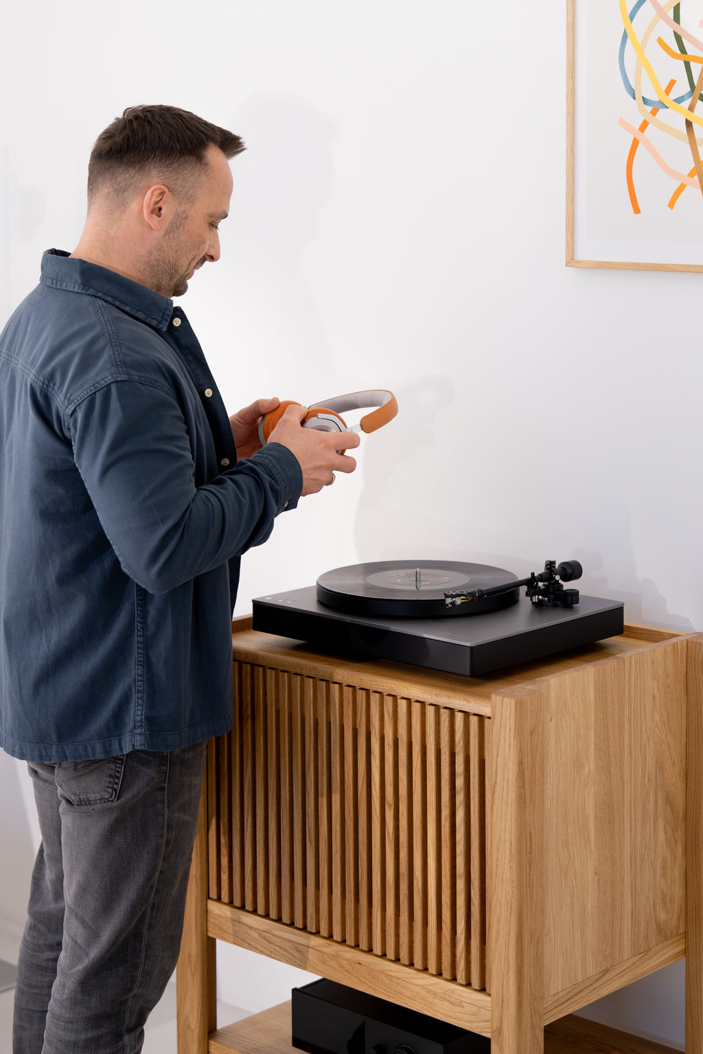 Man holding headphones next to a solid oak cabinet with a turntable.