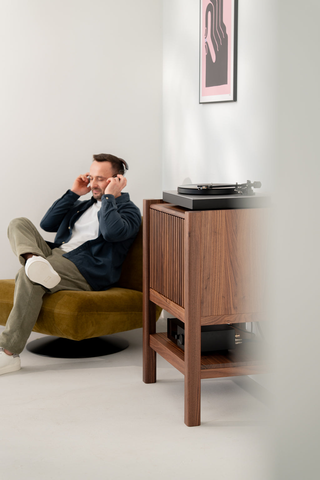 Man wearing headphones sitting next to a solid walnut wood cabinet with a turntable on top.