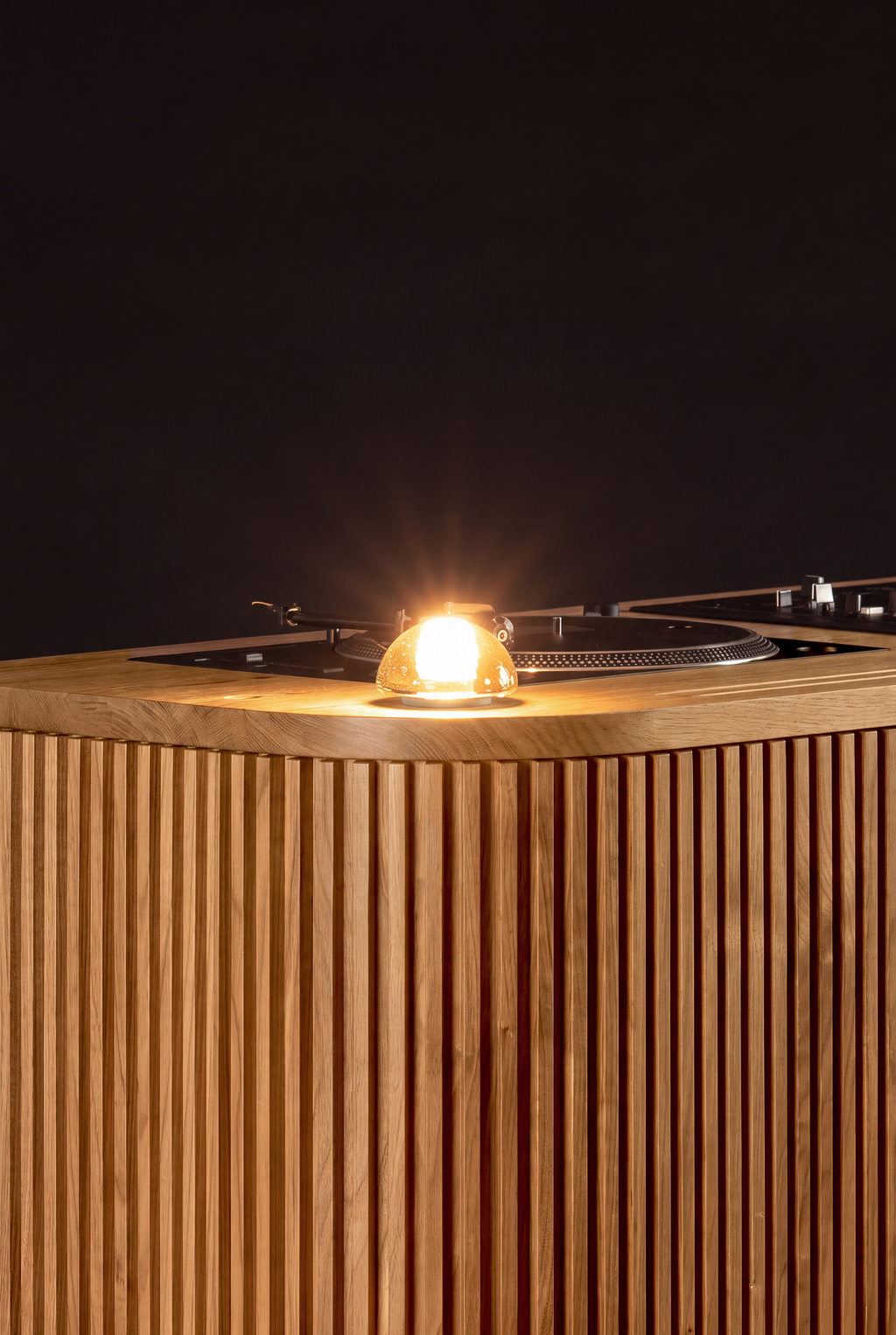 LOOP in solid oak, with a glowing glass lamp above the vertically grooved corner against a dark background