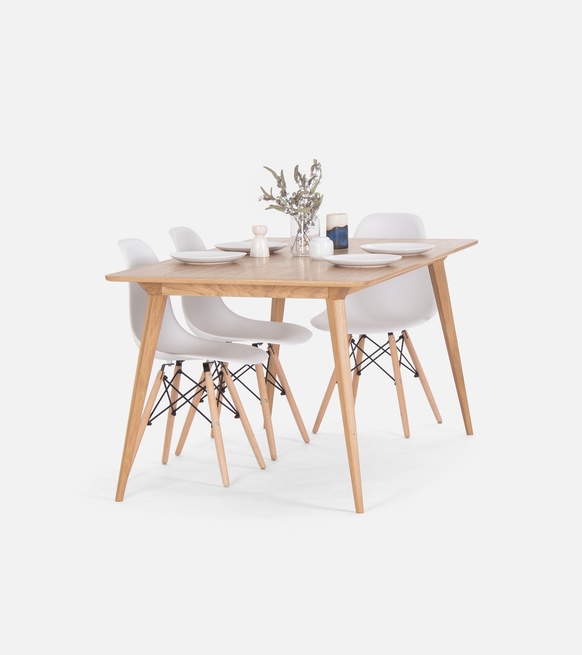 Wooden dining table set with four white chairs, set with plates and a small flower vase.