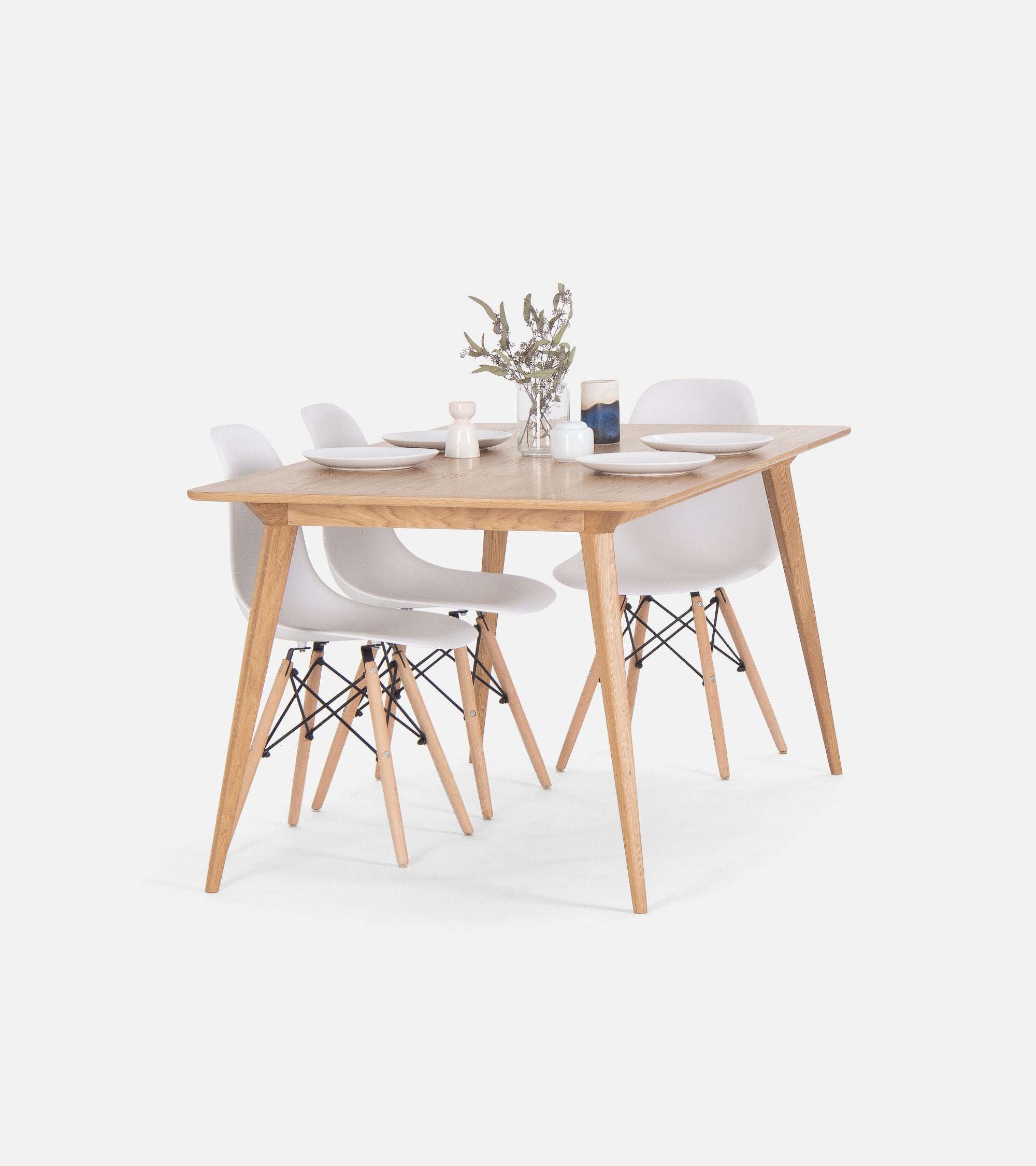 Wooden dining table set with four white chairs, set with plates and a small flower vase.
