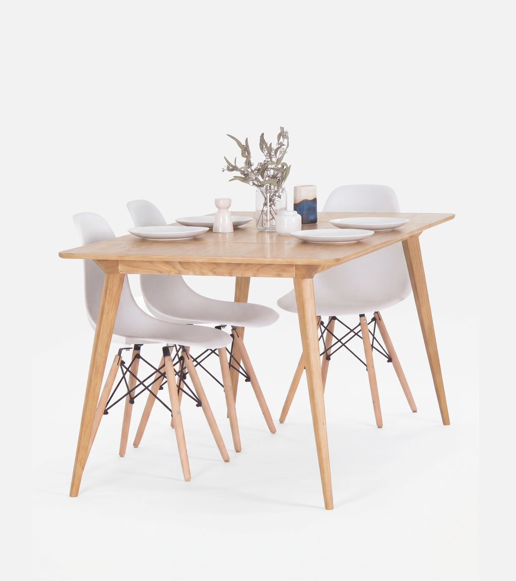 Wooden dining table set with four white chairs, set with plates and a small flower vase.