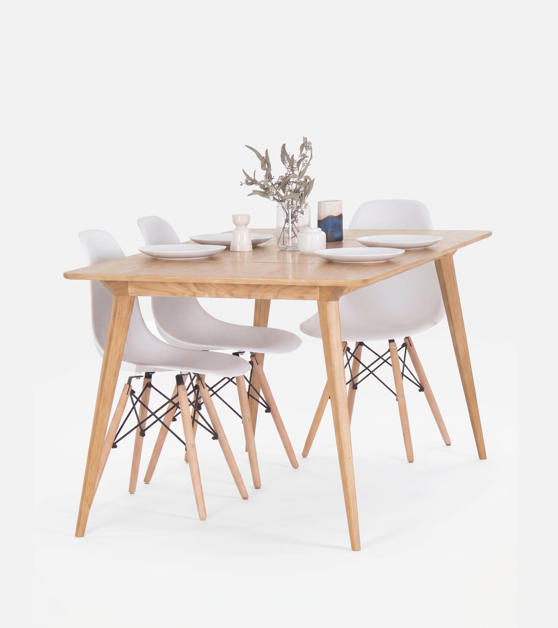 Wooden dining table set with four white chairs, set with plates and a small flower vase.