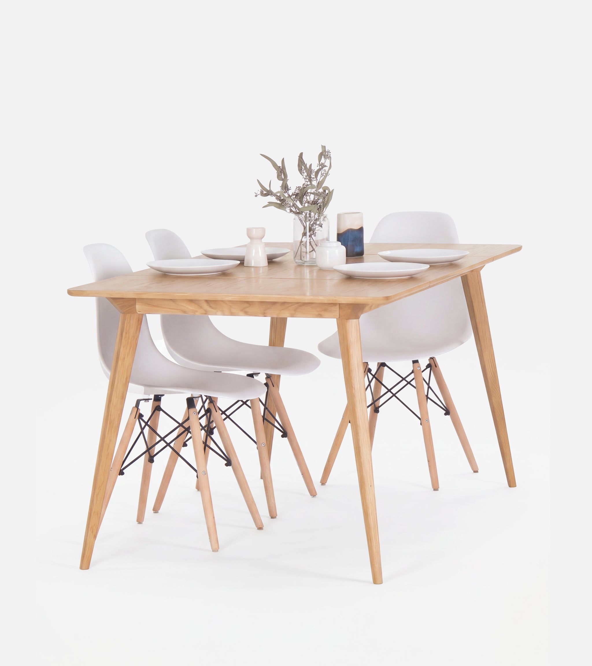 Wooden dining table set with four white chairs, set with plates and a small flower vase.