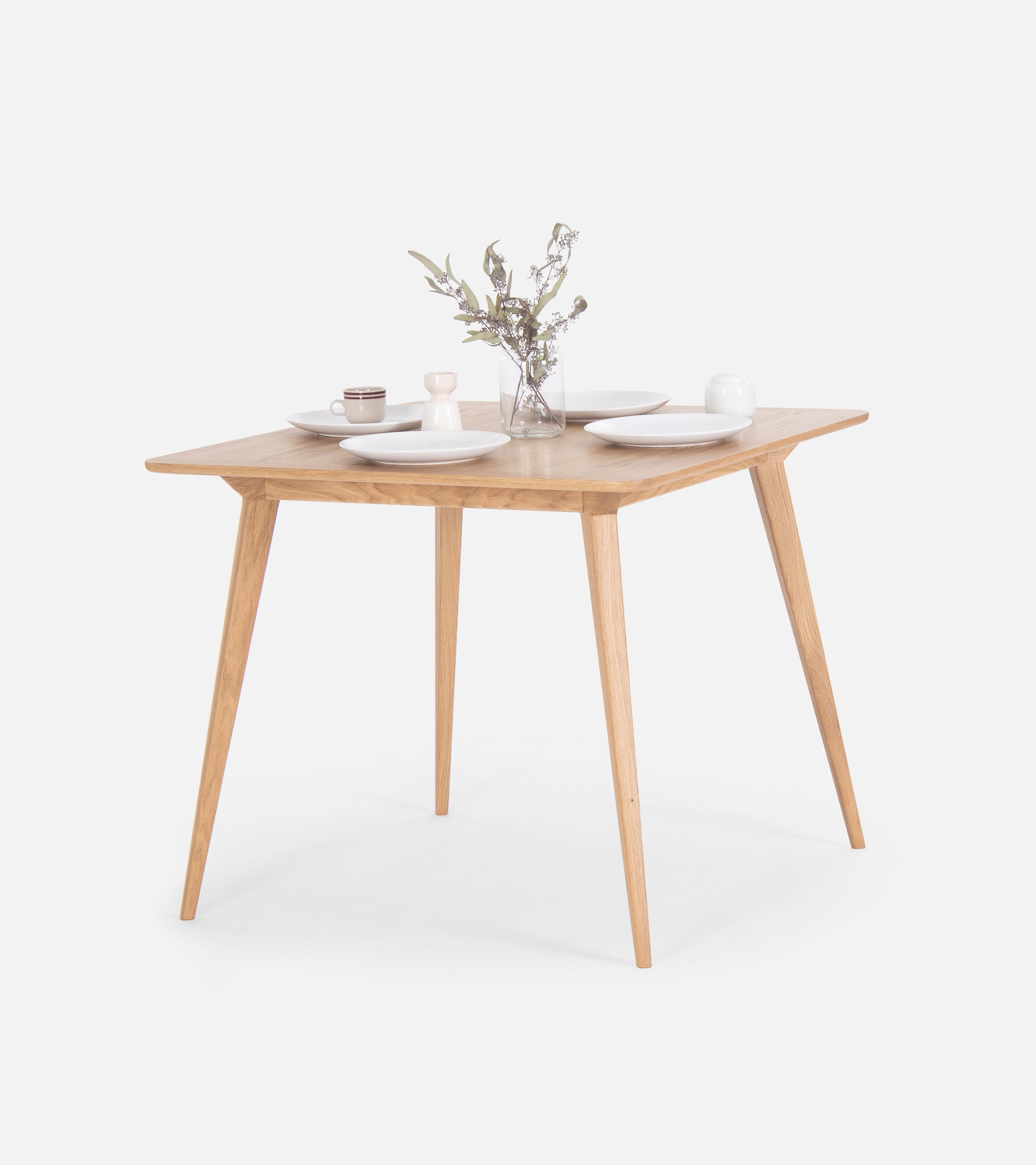 Square wooden table with dishes and a vase of flowers.