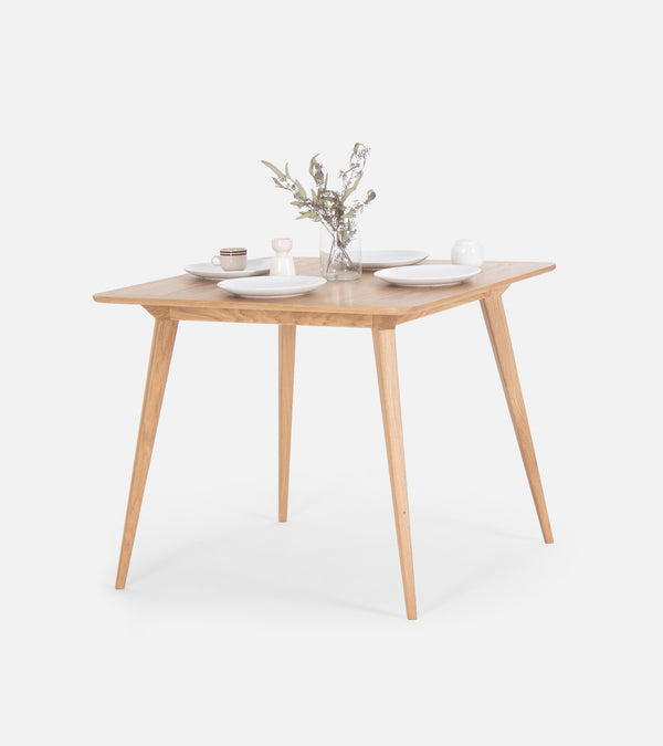 Square wooden table with dishes and a vase of flowers.