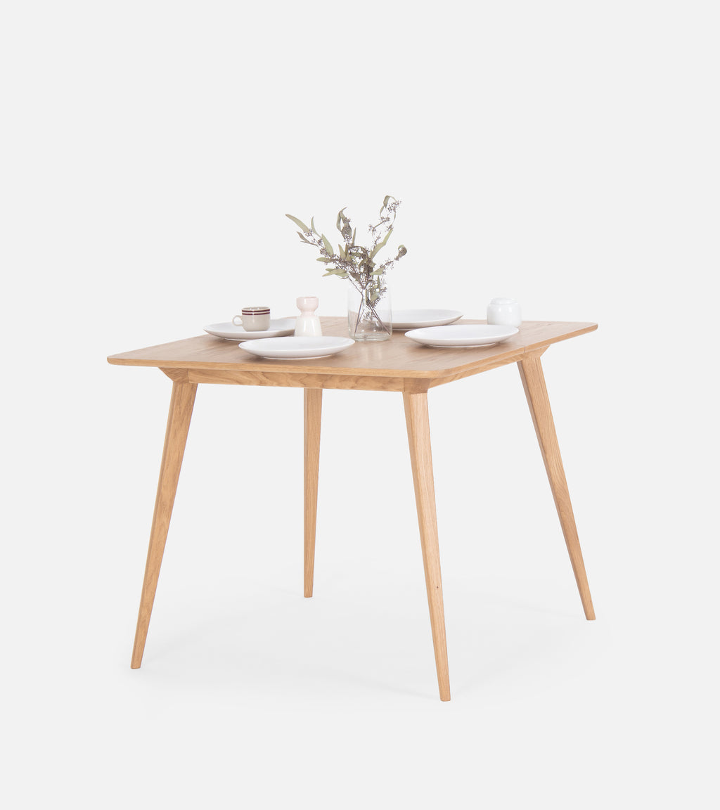 Square wooden table with dishes and a vase of flowers.