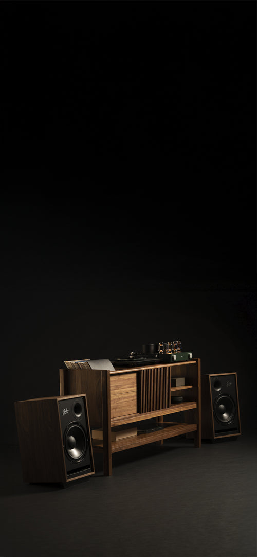 A modern wooden audio setup features a turntable and amplifier on a central console with shelving. Two speakers stand on either side, surrounded by darkness. The unit's minimalist design highlights its sleek and vintage style, complemented by a collection of vinyl records.