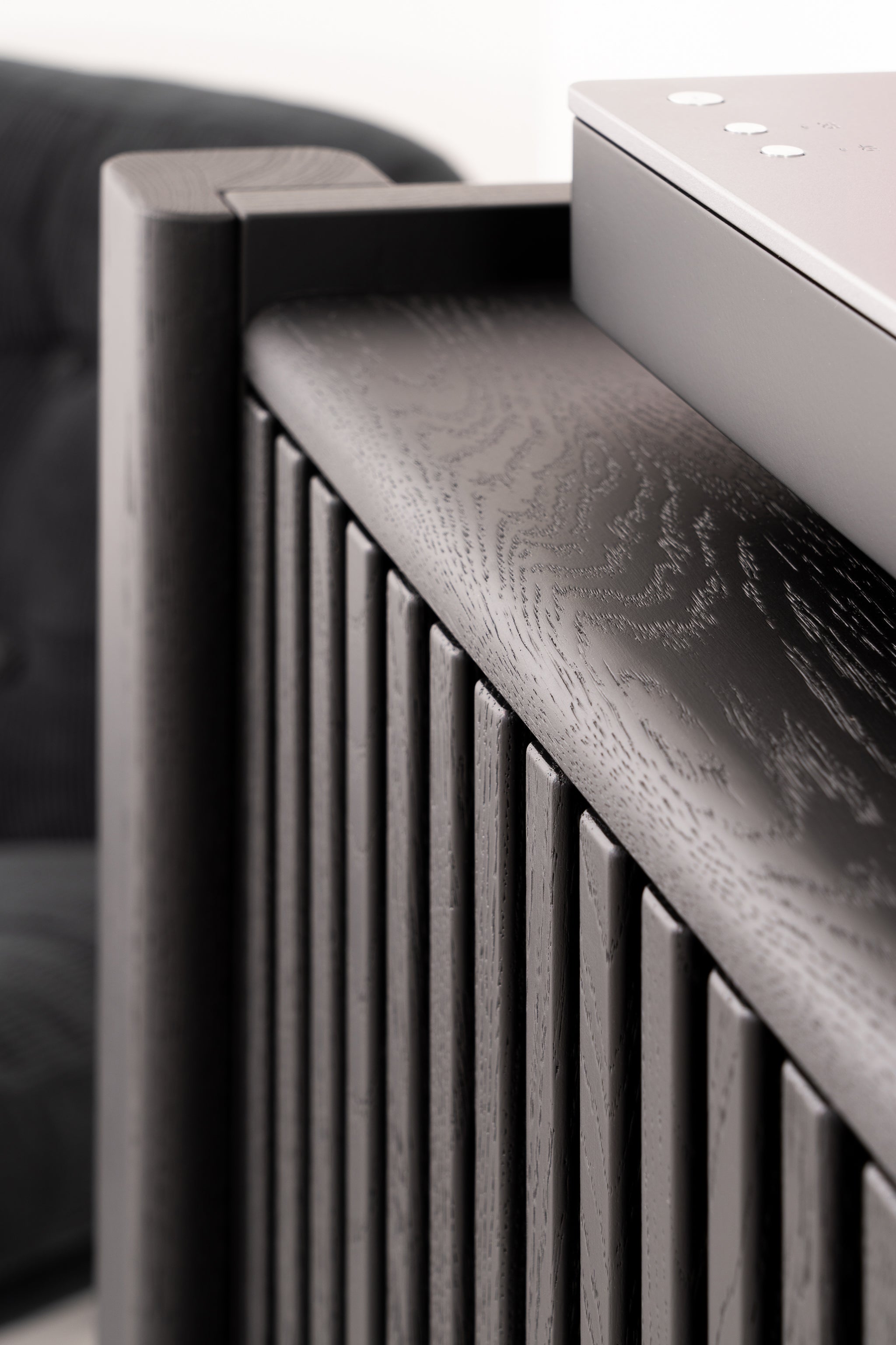 Close-up of a modern, dark wood slatted design with a smooth metallic surface on top.