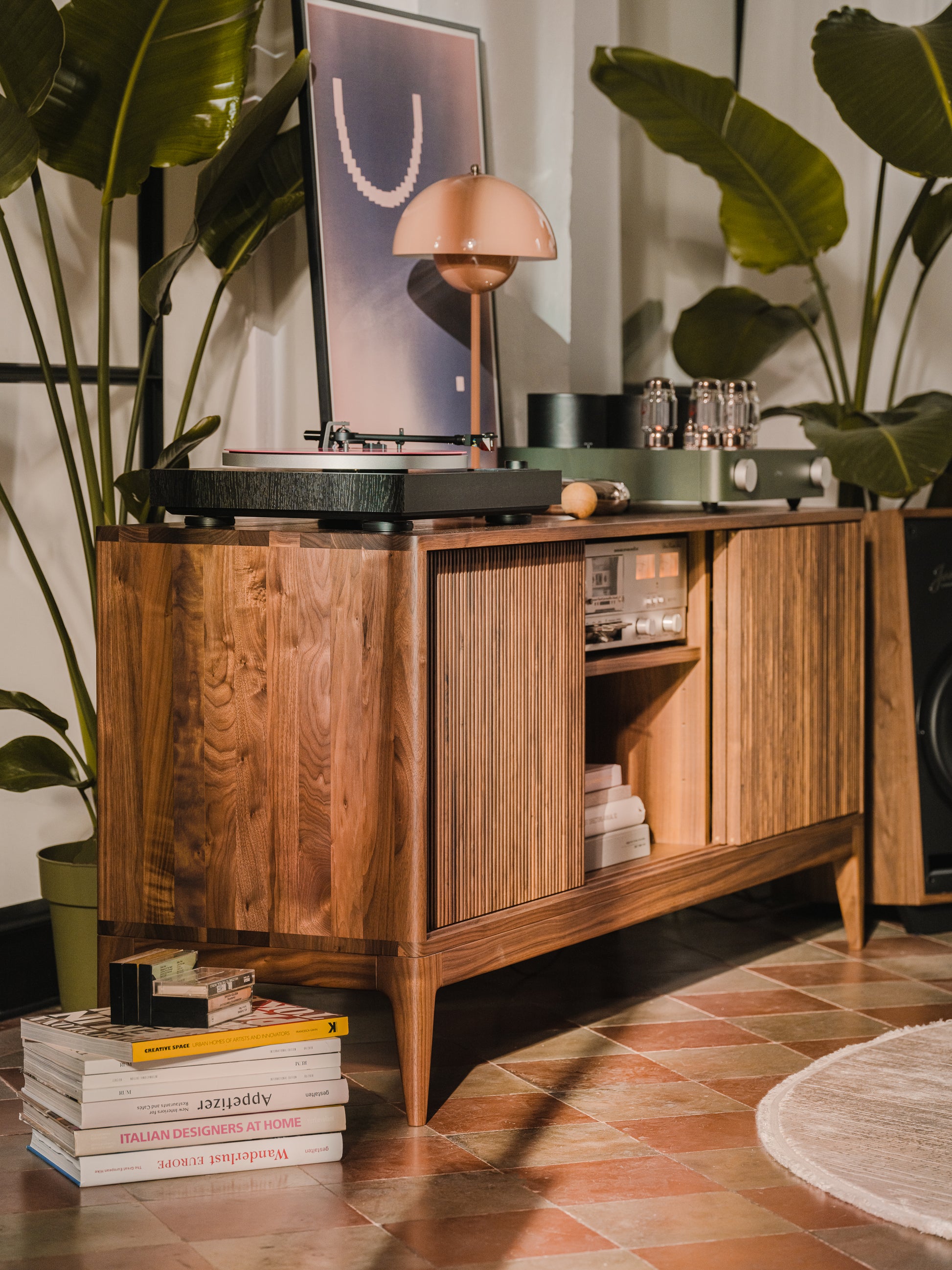 Mid-century console with a record player, ambient lamp, and plants. Books are stacked on the floor.
