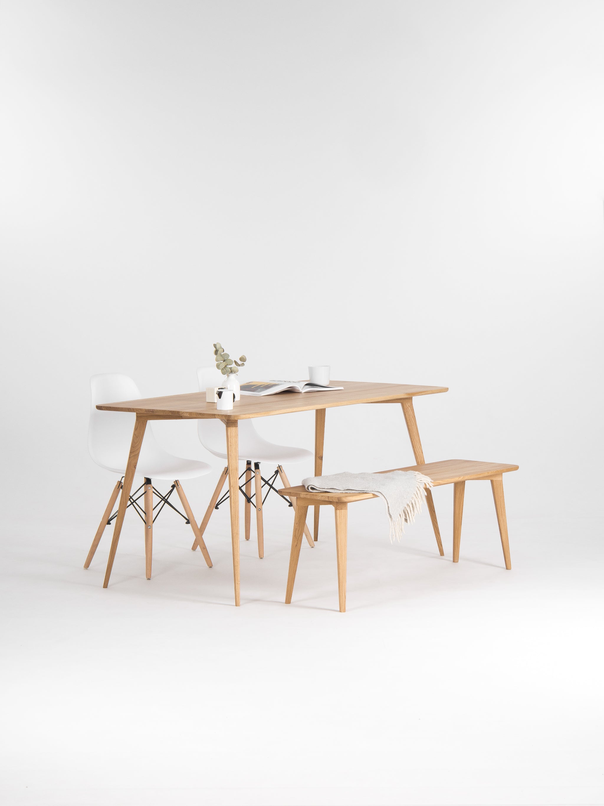 Minimalist dining setup with a wooden table, white chairs, a bench, a vase, and a cup.