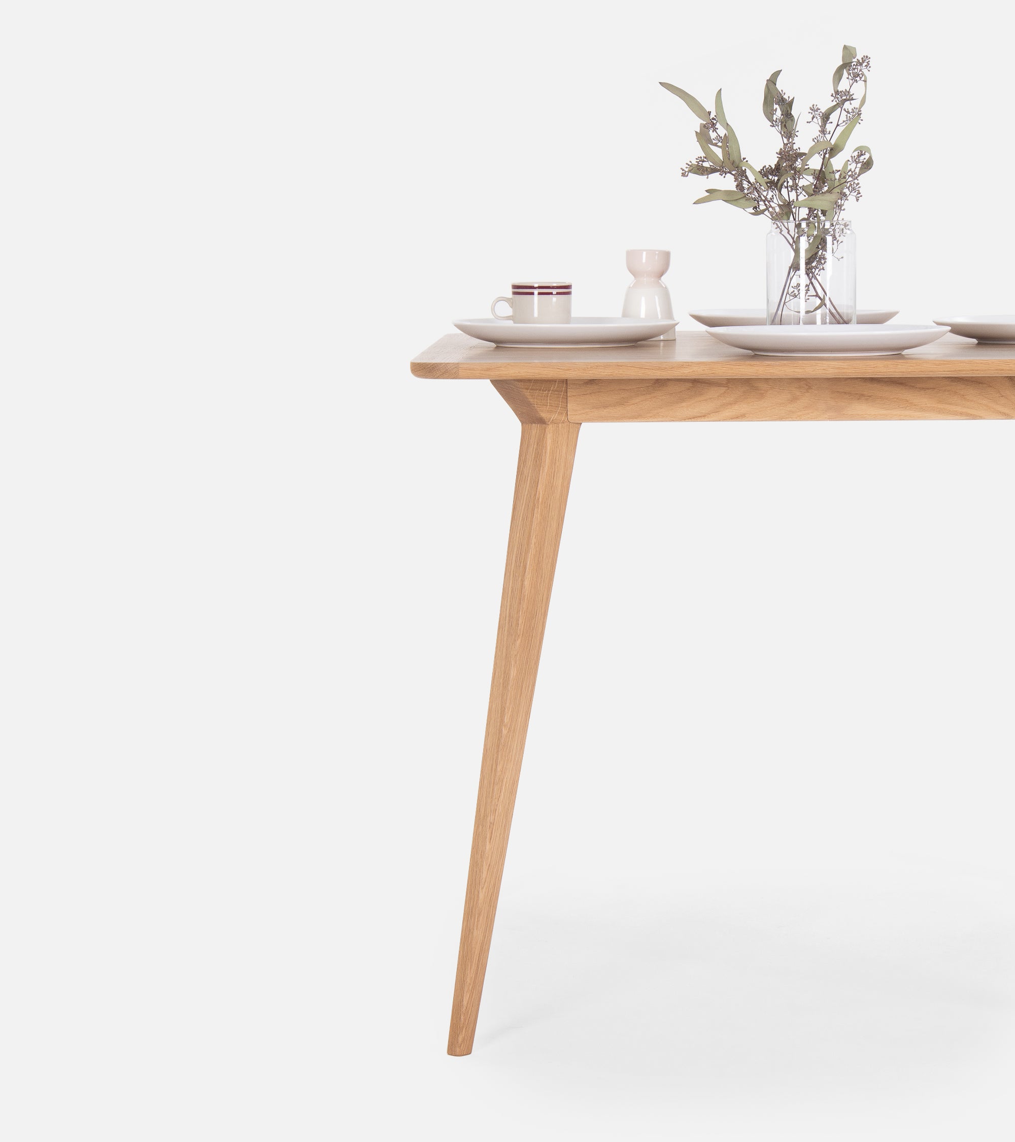 Minimalist wooden table with a vase, cup, and plates set on top.