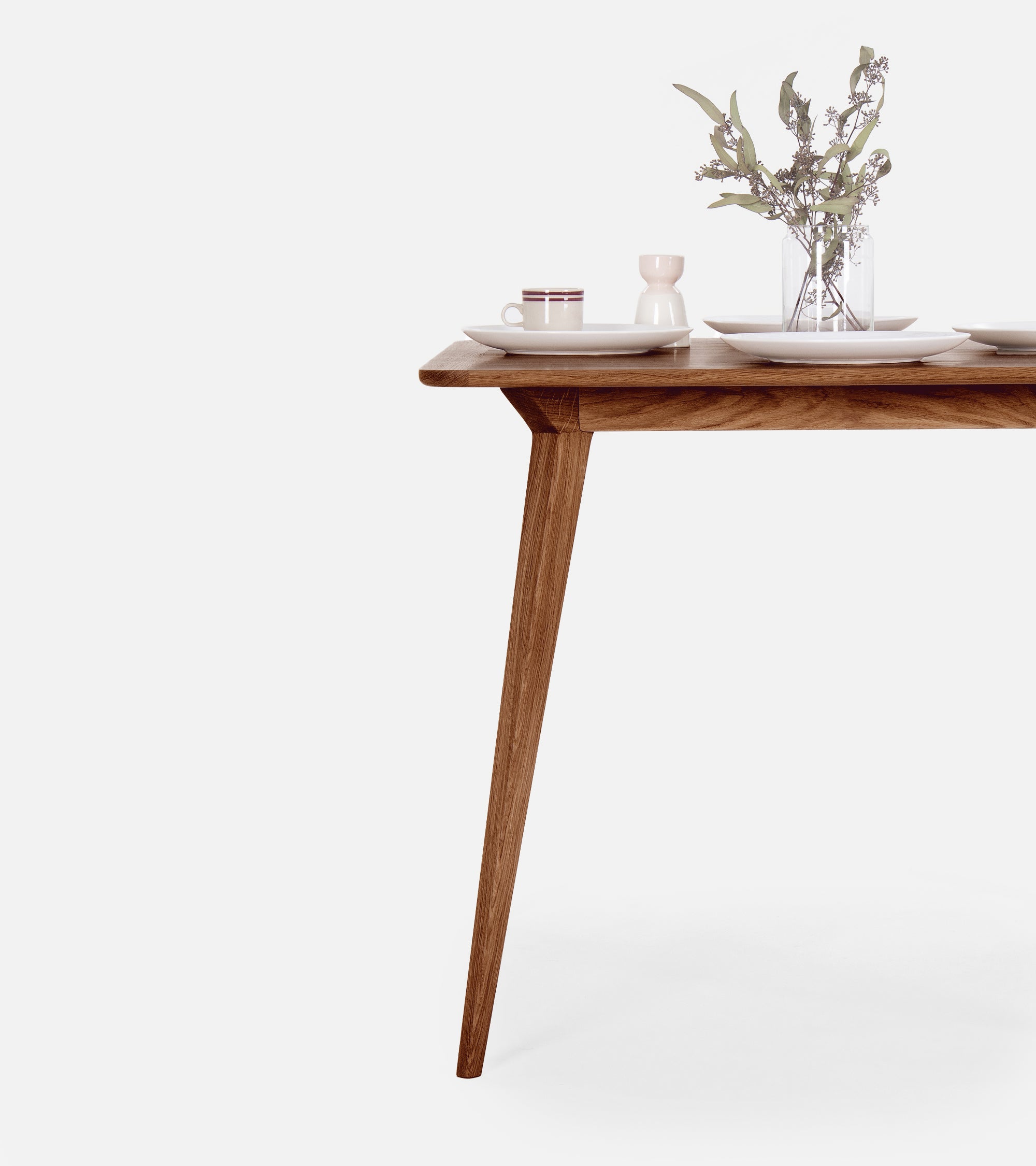 A wooden dining table set with two white chairs, a vase with flowers, and crockery.