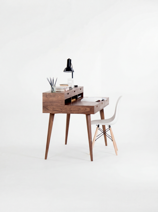 Minimalist wooden desk with a white chair, black lamp, and books against a white background.