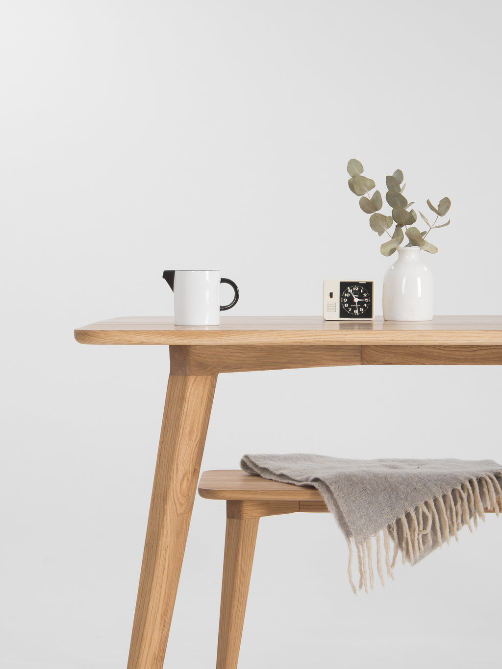 Minimalist wooden table with a vase, clock, mug, and draped blanket.