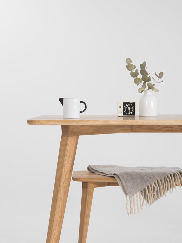 Minimalist wooden table with a vase, clock, mug, and draped blanket.