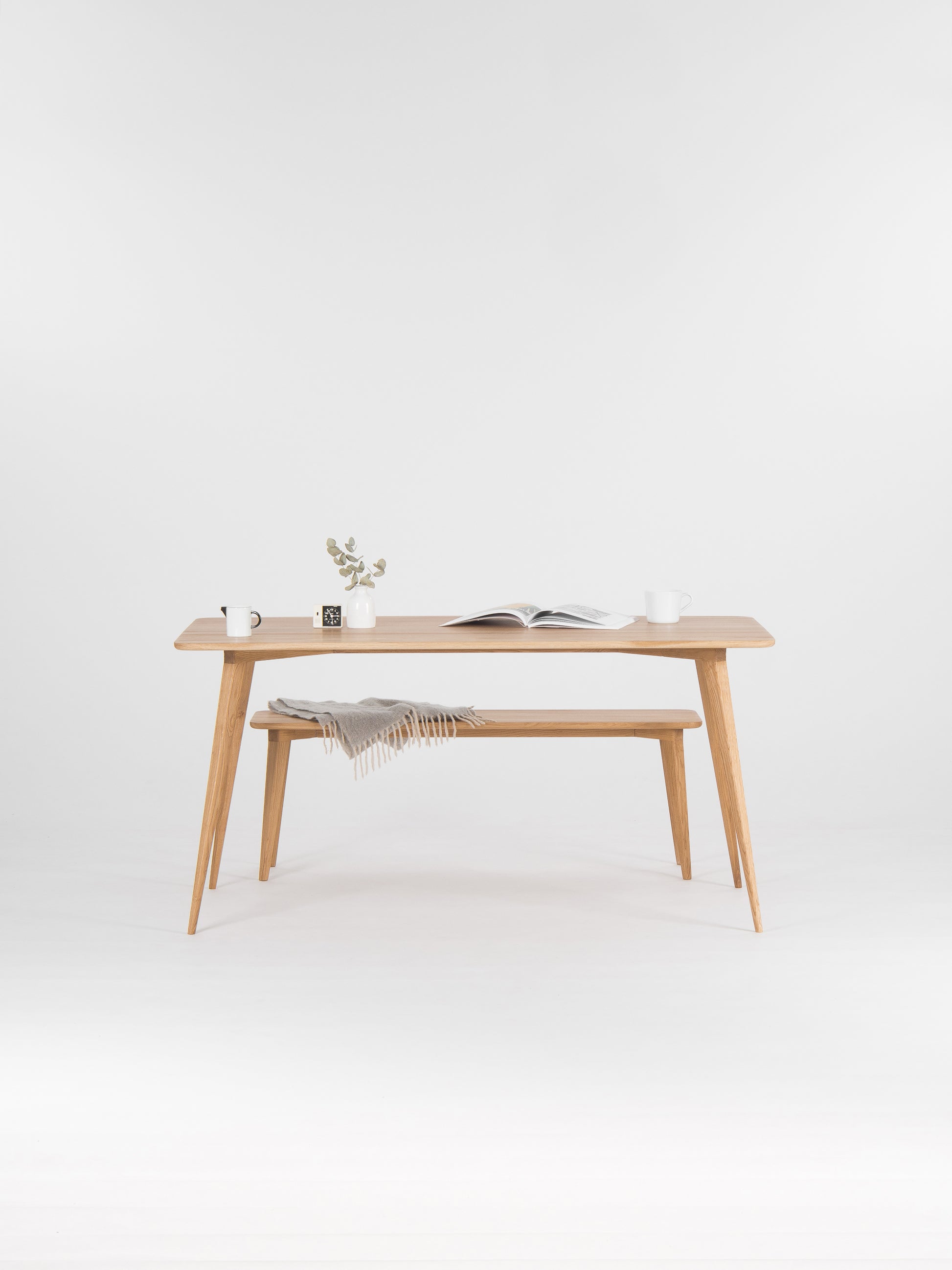 Minimalist wooden table with books, mugs, and a vase, against a plain white background.