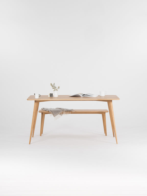 Minimalist wooden table with books, mugs, and a vase, against a plain white background.